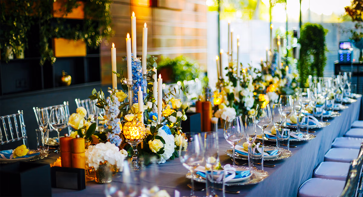 Long banquet table set with candlelight and yellow floral centerpieces under string lights
